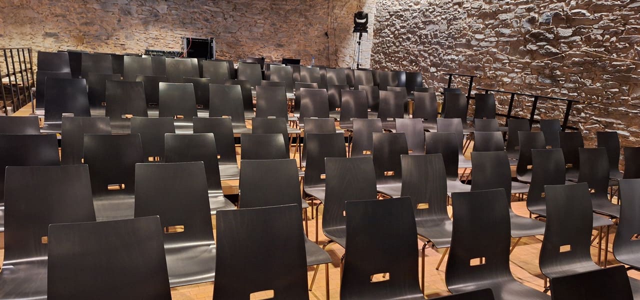 Bestuhlter Saal für Veranstaltungen in der Pfarrscheune Igstadt Reihen aus modernen, dunkelbraunen Holzstühlen in der Pfarrscheune Igstadt, aufgestellt für eine Veranstaltung vor einer historischen Natursteinwand
