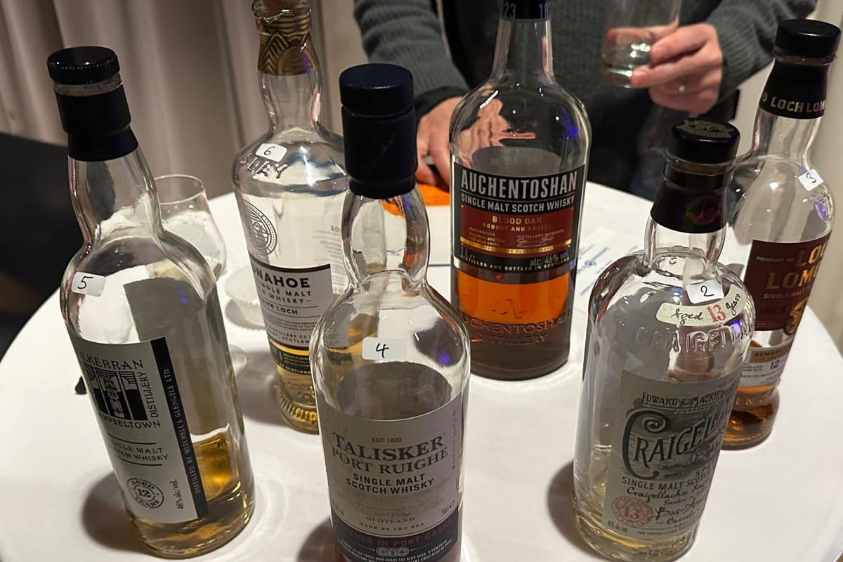 Sechs verschiedene, teilweise geleerte schottische Whisky-Flaschen (darunter Talisker und Auchentoshan) mit weißen Nummerierungsaufklebern stehen auf einem weiß gedeckten Stehtisch beim Tasting in der Pfarrscheune Igstadt